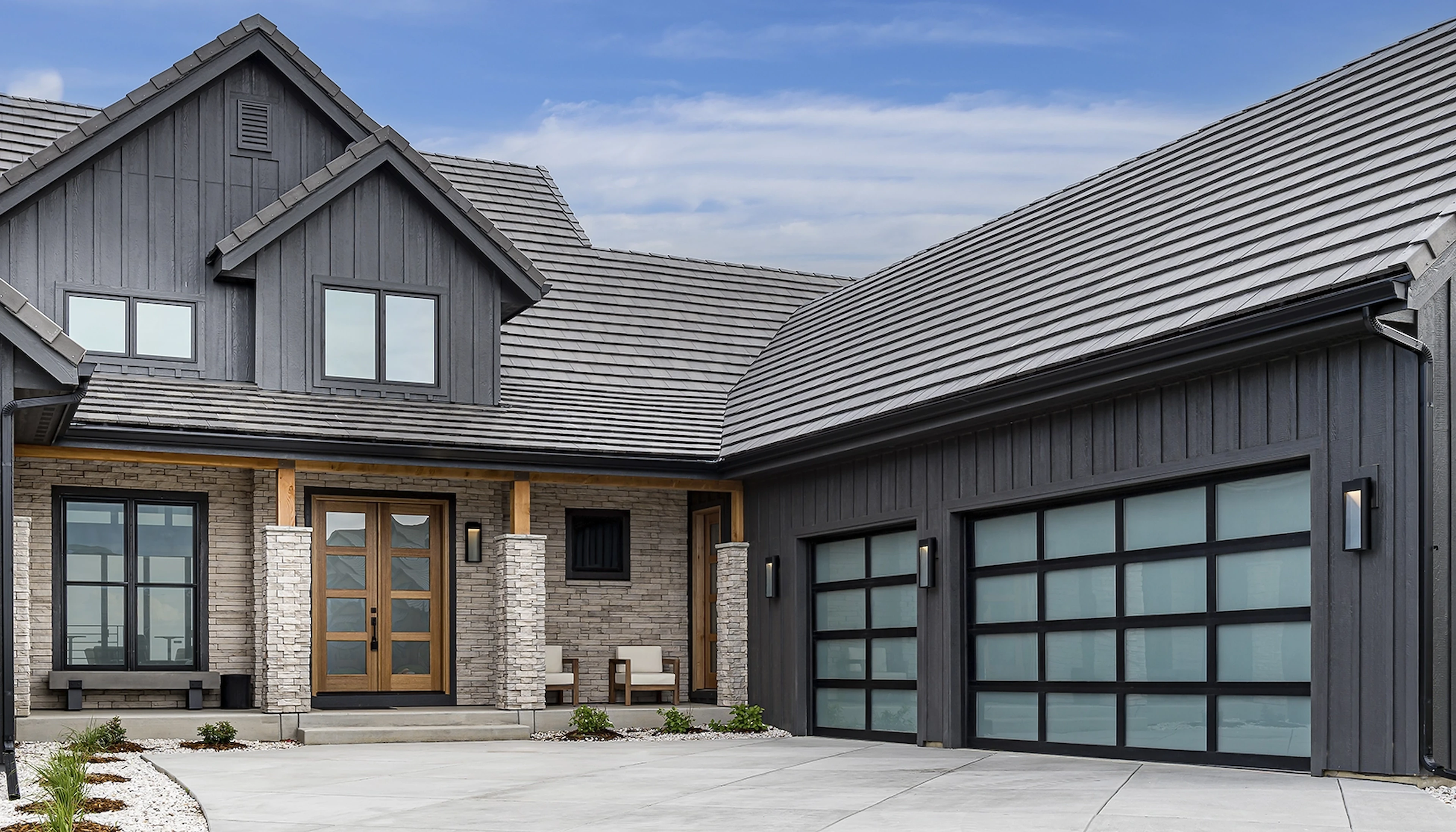 Modern grey home with two black framed glass garage doors on a wide concrete driveway